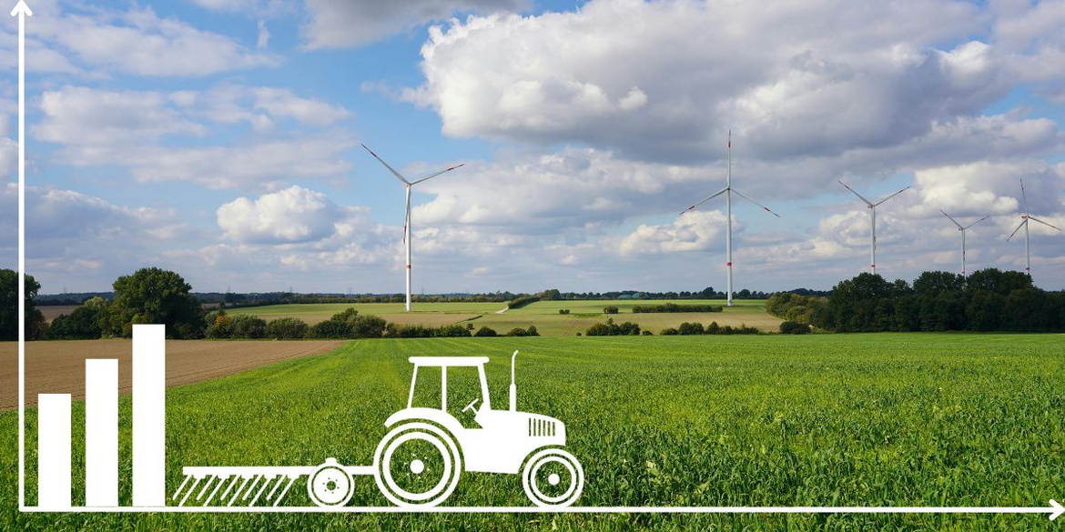 Traktor vor einer Wiese und Windrädern