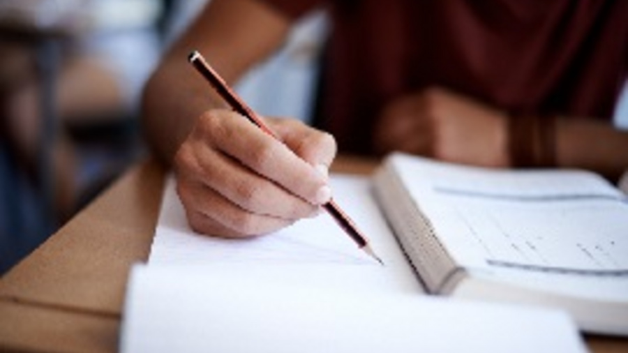 Person sitzt am Schreibtisch und liest in einem Buch und macht sich Notizen